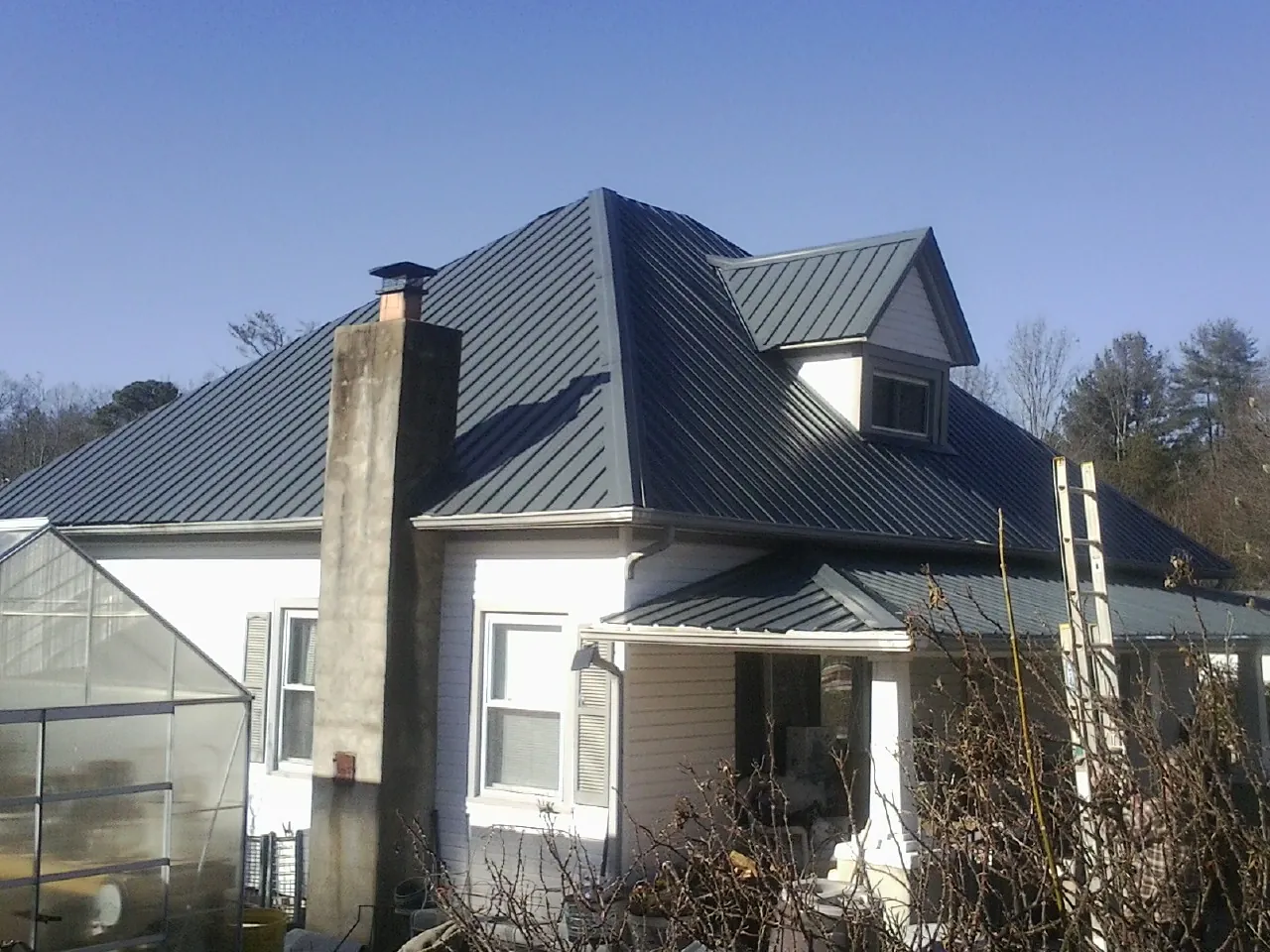 Dark blue standing seam metal roof on a white farmhouse with dormer — Slate & Tile Roof Repair by Roofing Brothers in Presto