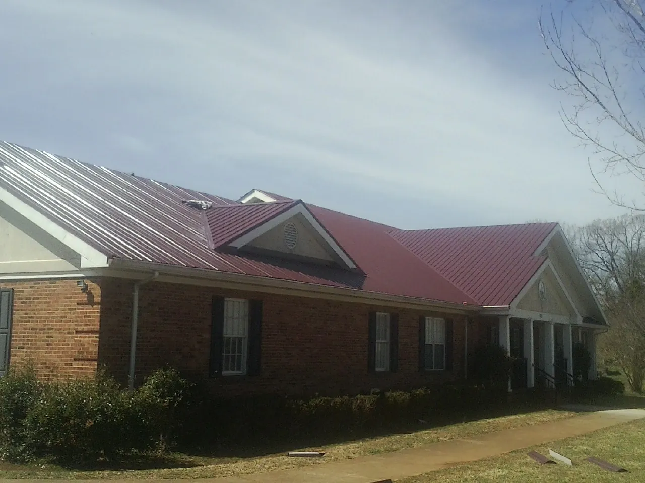 Red metal roof with gabled entries on a long brick building, from a Hail Damage Roof Repair job in Presto
