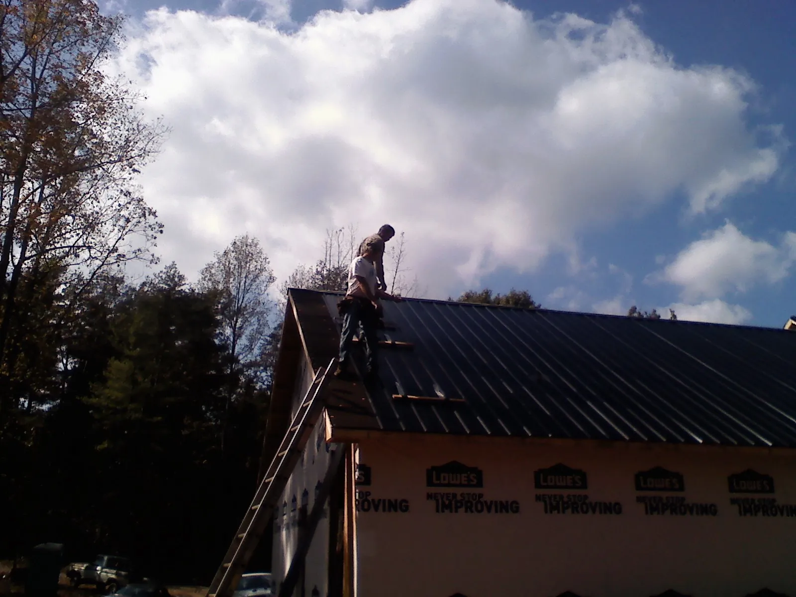 Roofer fastening dark metal panels high against a cloudy sky, from a Roof Inspection job in Presto